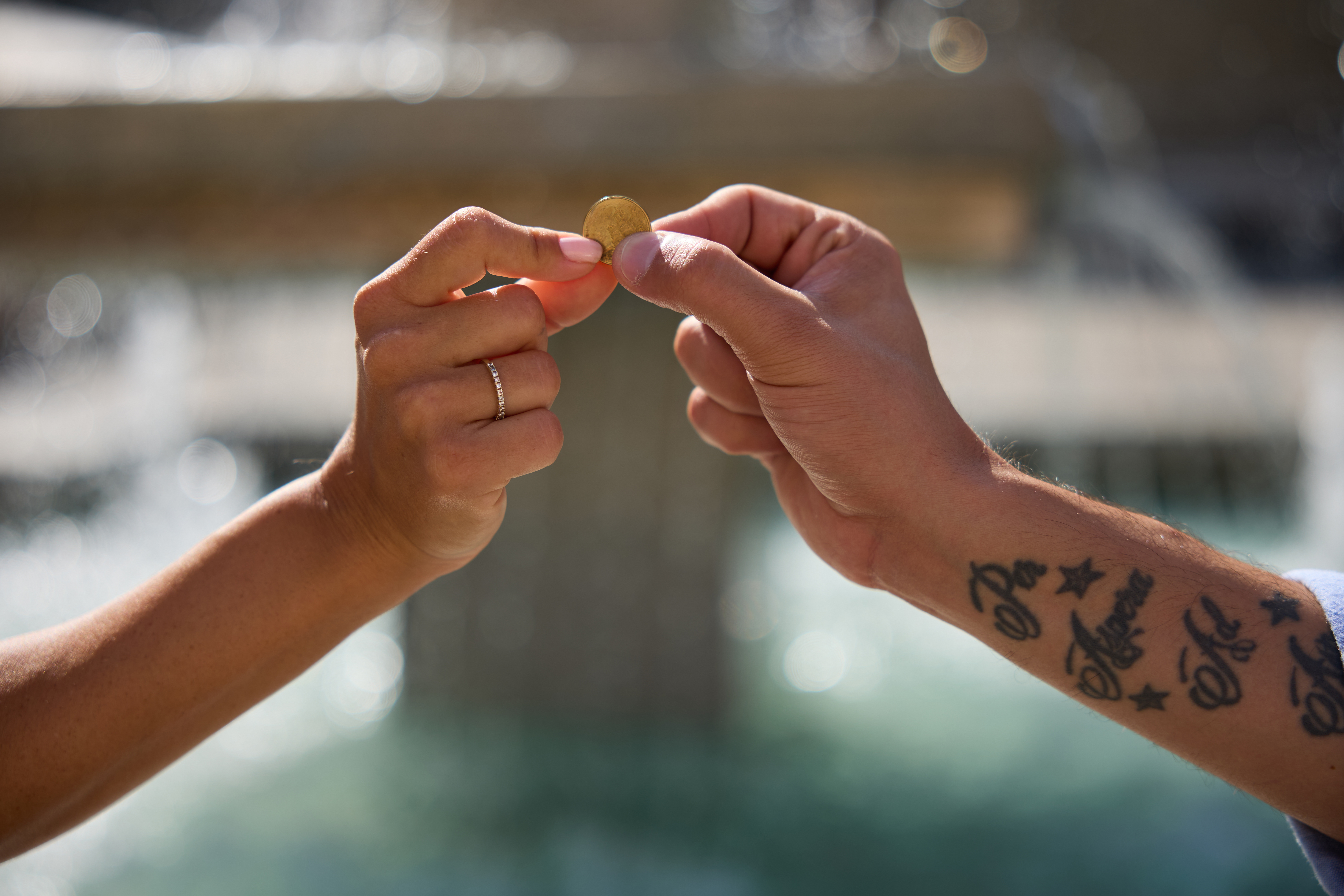Two people holding a coin together, preparing to toss it into a fountain for a wish